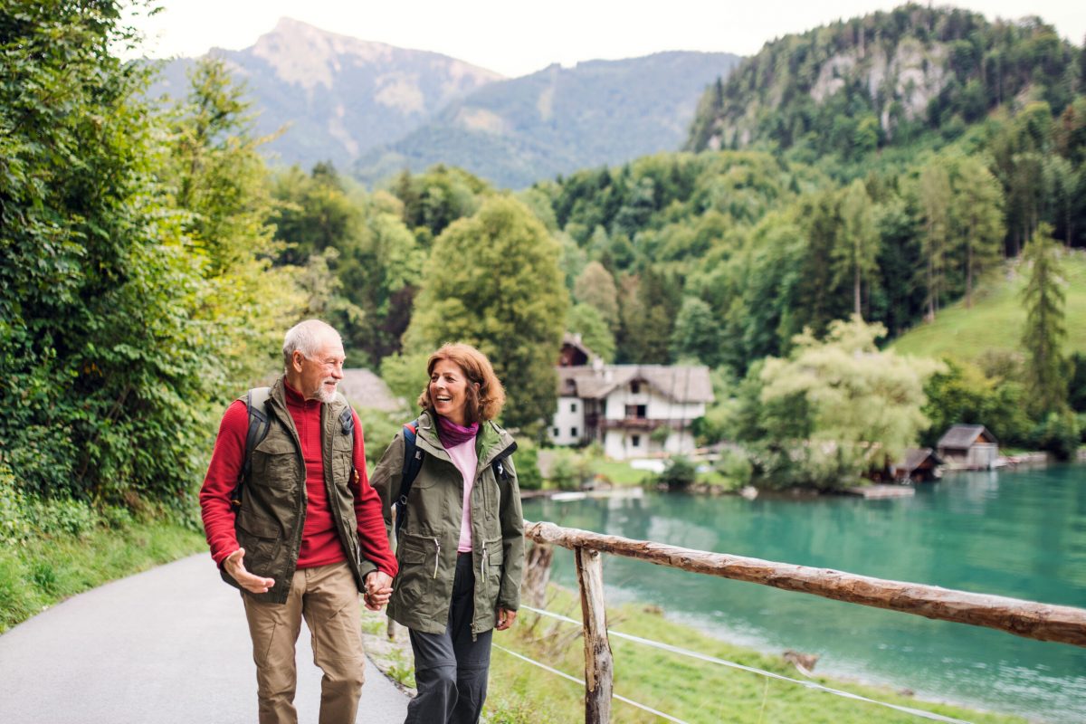 An active senior pensioner couple hiking in nature, holding hands.